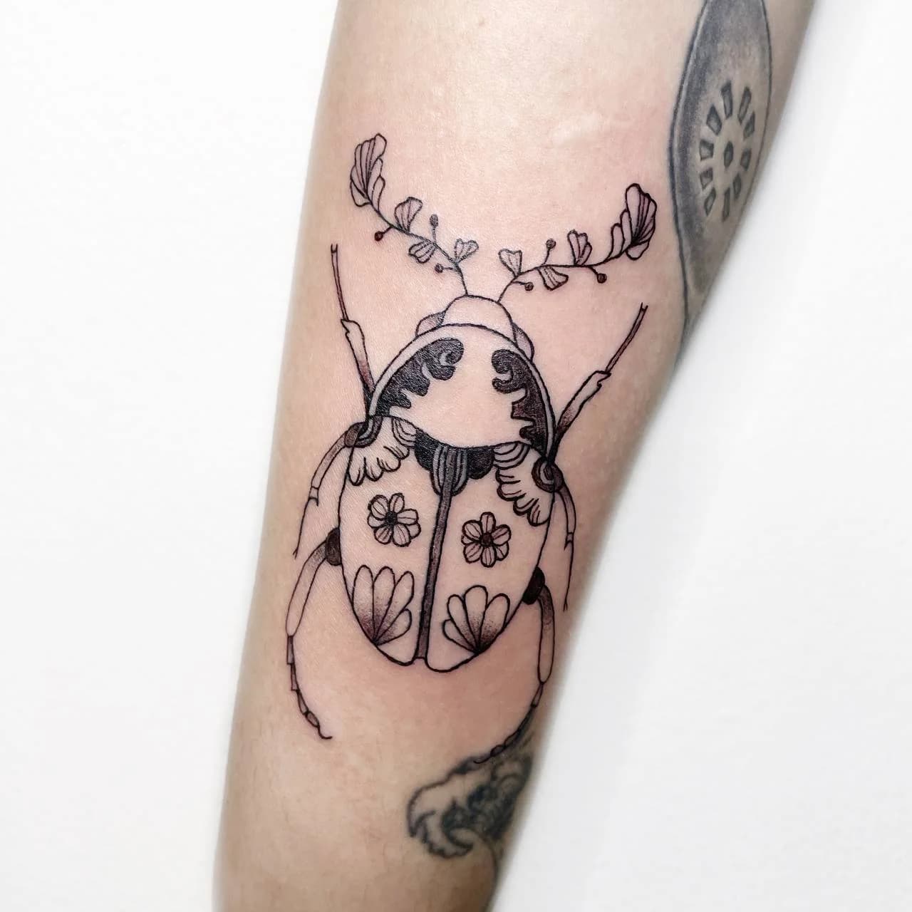 Botanical beetle tattoo on the forearm by Nika Osseili.