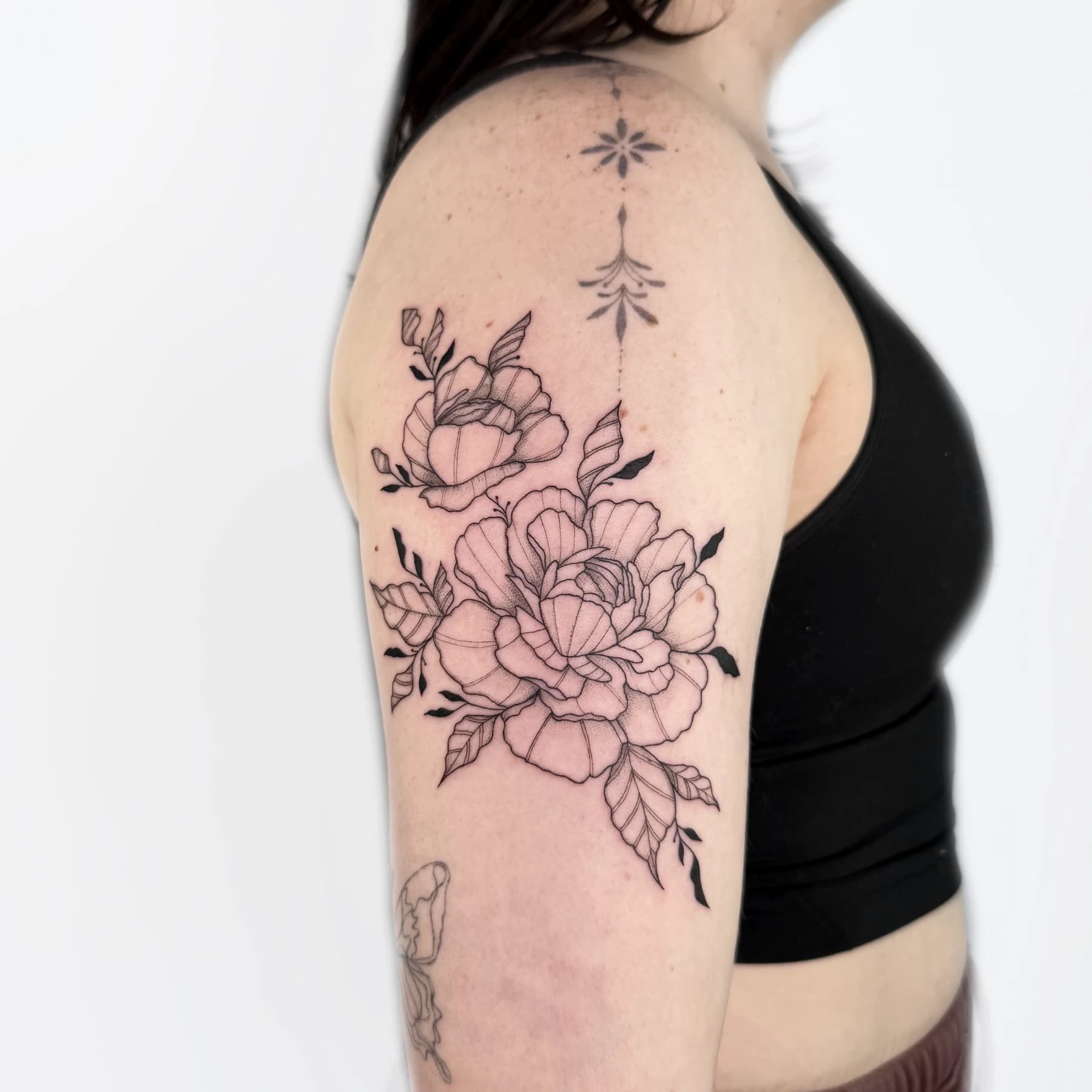 Botanical fine line tattoo on the shoulder by Ukrainian tattoo artist Nika Osseili.