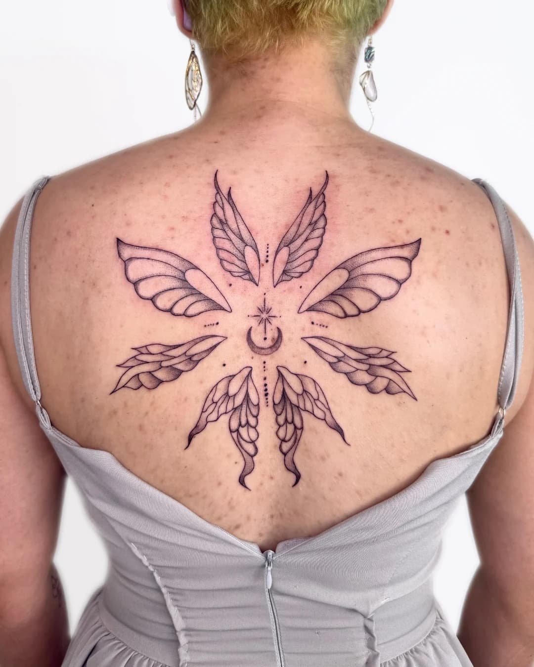 Moth-inspired fine line tattoo on the upper back by Nika Osseili.