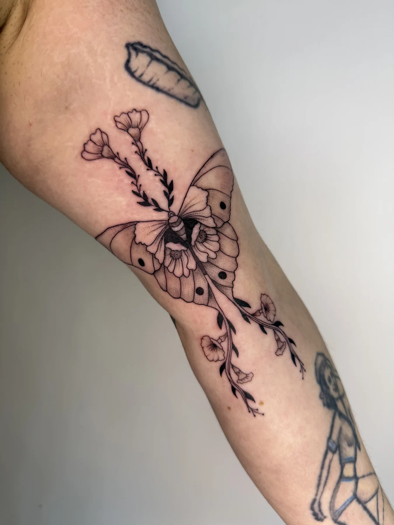 Moth and floral tattoo on the forearm by Nika Osseili.