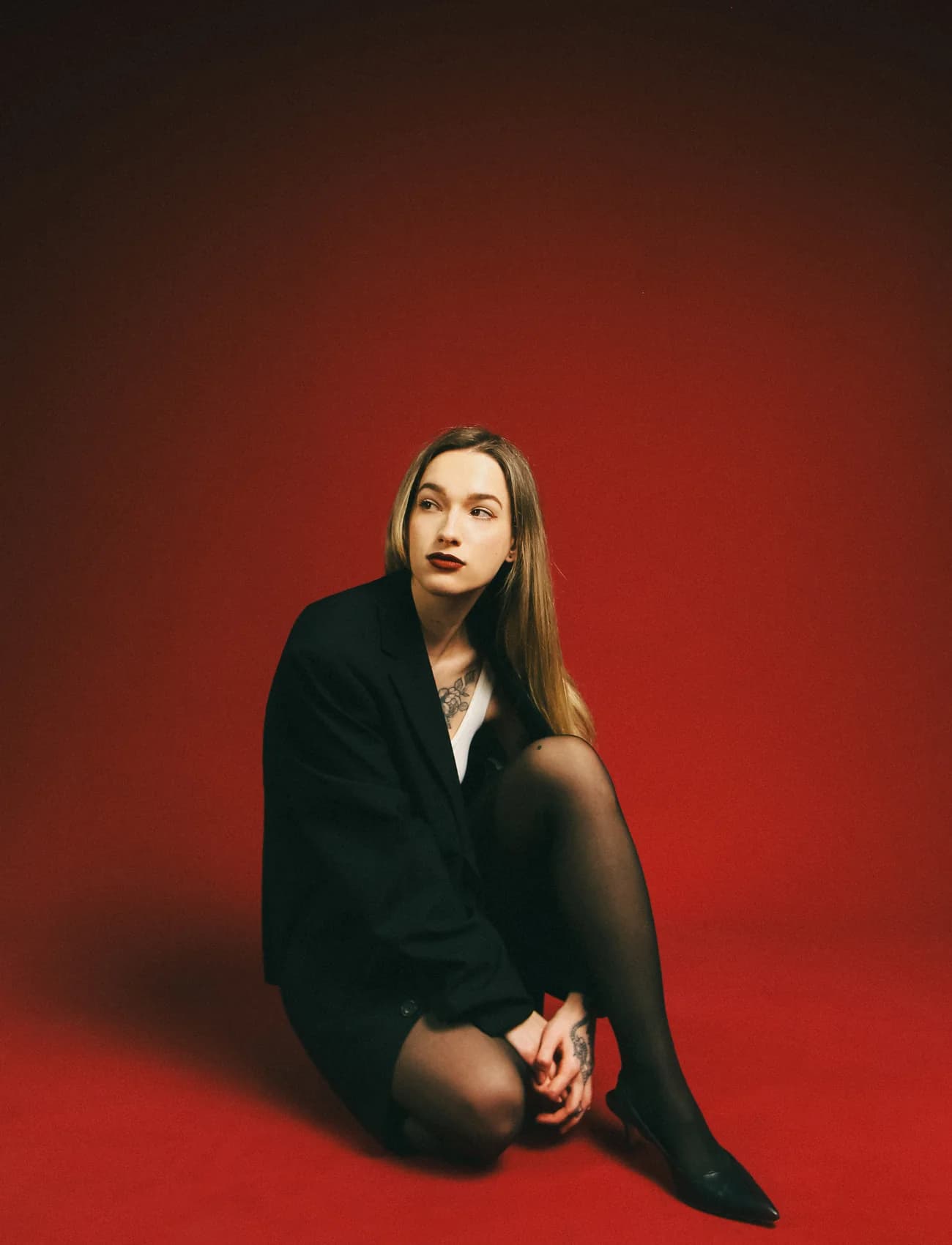 Editorial seated portrait of Nika Osseili on a red studio set.